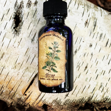 A filled dark blue bottle with a label reading "Persephone Naturals, Allergy, Ingredients: nettles, goldenrod, vodka."   