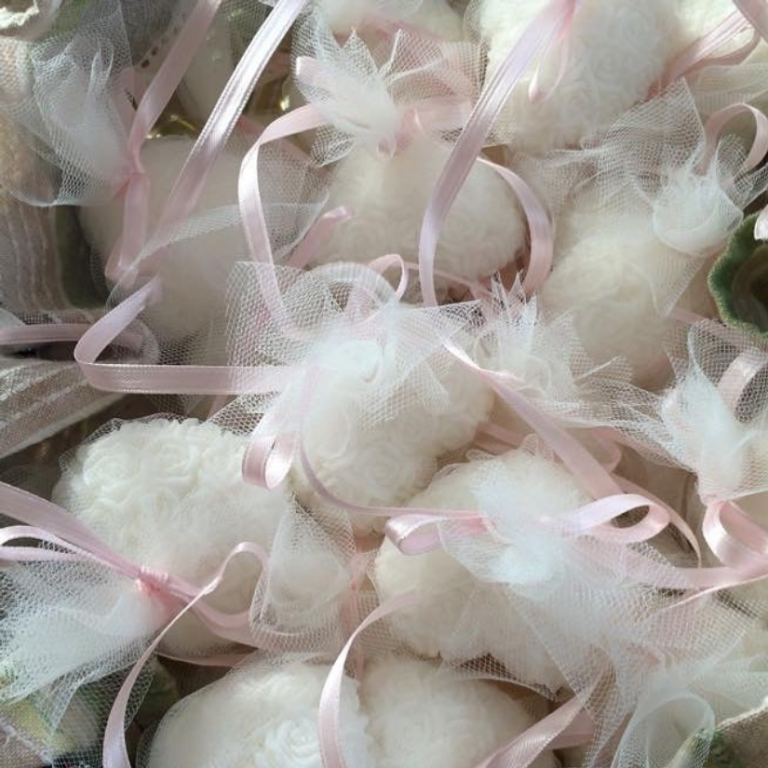 A pile of white heart soaps with rose detailing, each wrapped white tulle and pink ribbon.